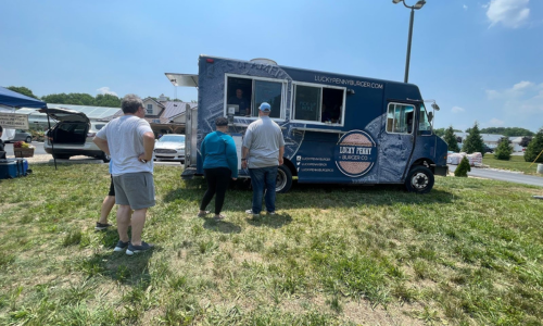Customers lined up on a sunny day, waiting to order at the Lucky Penny Burger Co. food truck.