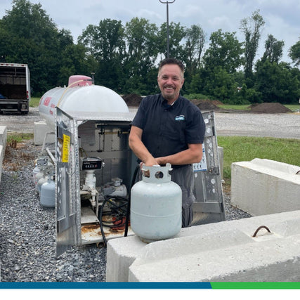 Propane RefillsA smiling employee holding a propane tank in front of a propane filling station at an outdoor location.